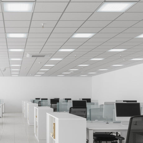 A modern office with empty workstations, each equipped with a chair and a computer. The space is well-lit with fluorescent ceiling lights and features a clean, minimalist design with white walls and tiled flooring.