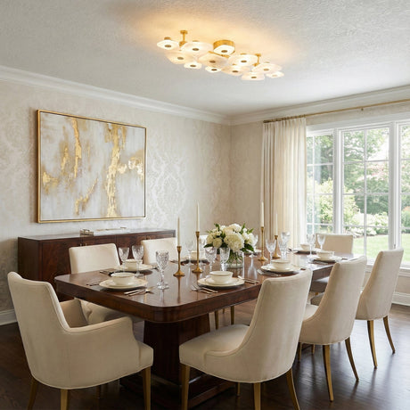 Elegant dining room with a wooden table set for eight, cream upholstered chairs, a floral centerpiece, large window with curtains, abstract gold artwork on the wall, and a modern chandelier overhead.