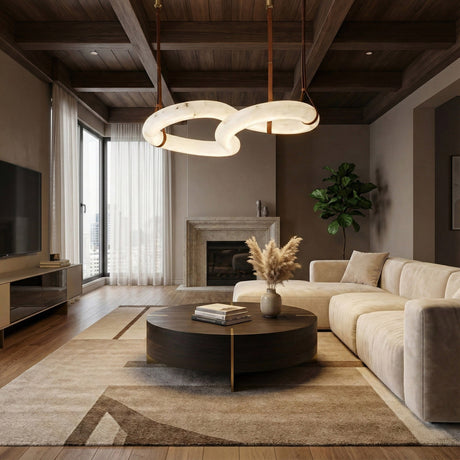 Modern living room with a beige sectional sofa, round dark coffee table, pampas grass vase, large abstract chandelier, fireplace, flat-screen TV, and a tall plant by sheer floor-to-ceiling windows.