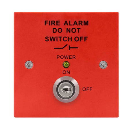 Close-up of a red fire alarm panel with a key switch. Text on the panel reads FIRE ALARM DO NOT SWITCH OFF. A central key slot is flanked by screws, with a green LED indicating POWER ON.