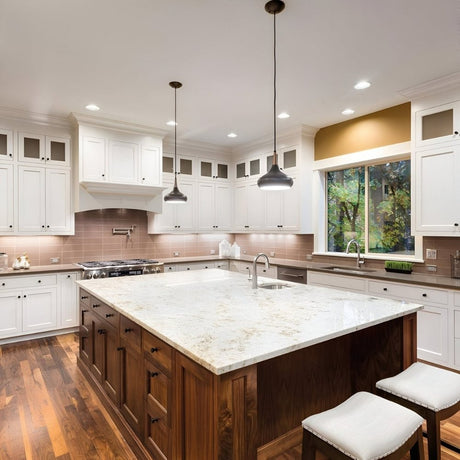 Spacious kitchen with white cabinets, marble island countertop, pendant lights, and warm wood flooring.