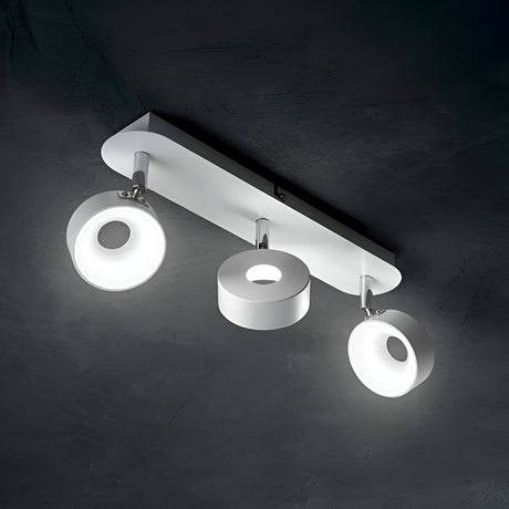 A modern ceiling light fixture with three white, circular lamps, each attached to a rectangular base. The lamps emit a bright white light against a dark background.