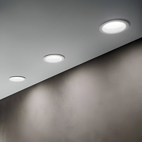 Ceiling with three round recessed lights casting soft illumination on a smooth, light-colored wall. The lights are evenly spaced, creating a modern and minimalist ambiance.