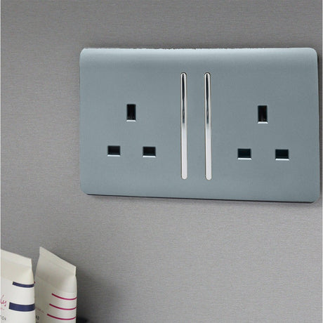 A cool grey double socket with chrome switches on a screwless plate, on a grey wall
