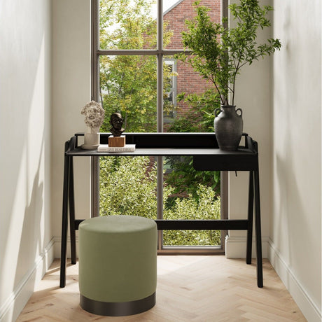 A black desk with a raised back shelf and a green stool in front of a tall window
