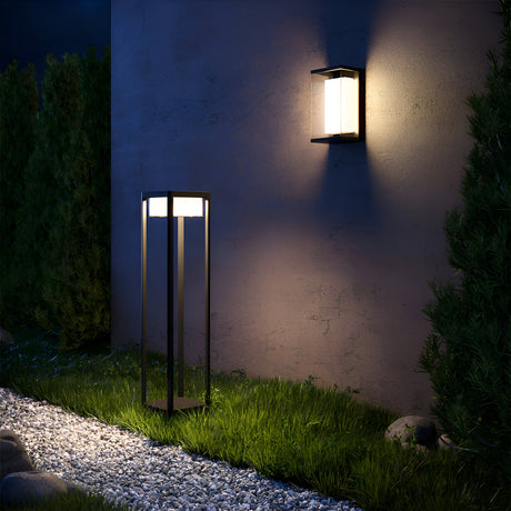 Outdoor lighting scene featuring a wall-mounted lantern and a tall garden lamp on a stone path. Both lights illuminate the lush grass and surrounding greenery at night.