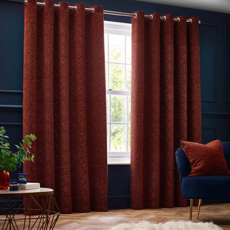 Galaxy Chenille Fully Lined Eyelet Curtains in copper, textured rust-toned fabric with silver eyelet heading, hung on a pole in a navy-walled living room beside a window.