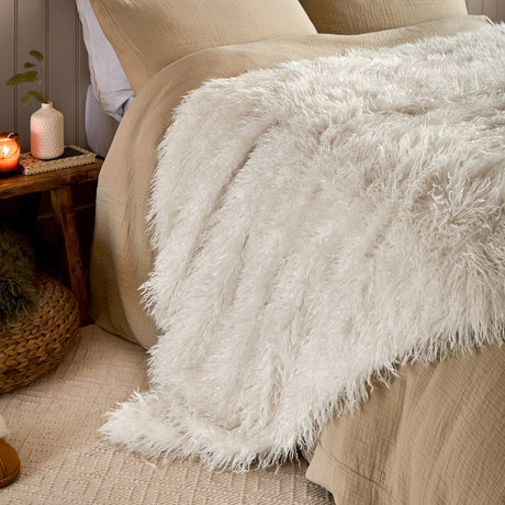 Cream long-pile faux fur throw across a made bed