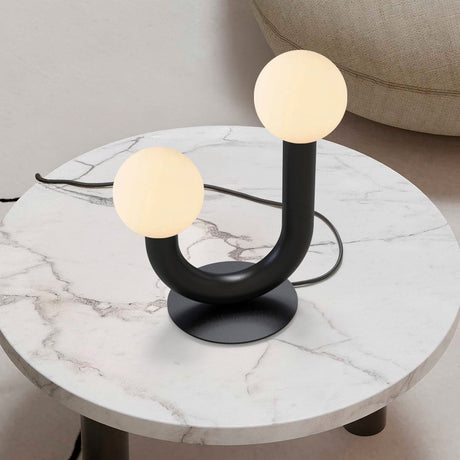 Rigoberta 2 Light Opal Glass Globe Table Lamp in matt black, curved U-shaped iron base with two uneven-height globes, shown on a marble side table.