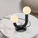 Rigoberta 2 Light Opal Glass Globe Table Lamp in matt black, curved U-shaped iron base with two globes at different heights, shown on a marble side table.