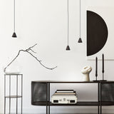 Rimini LED Cone Pendant Light in matt black, shown as three small conical shades on black cables at varied heights in a living room setting with a dark sideboard and decor.