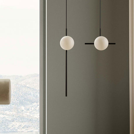 Roxanne North opal glass globe pendant lights in matt black, each with a slim rod, single 10cm globe and horizontal counterweight, shown against a grey wall near a window.