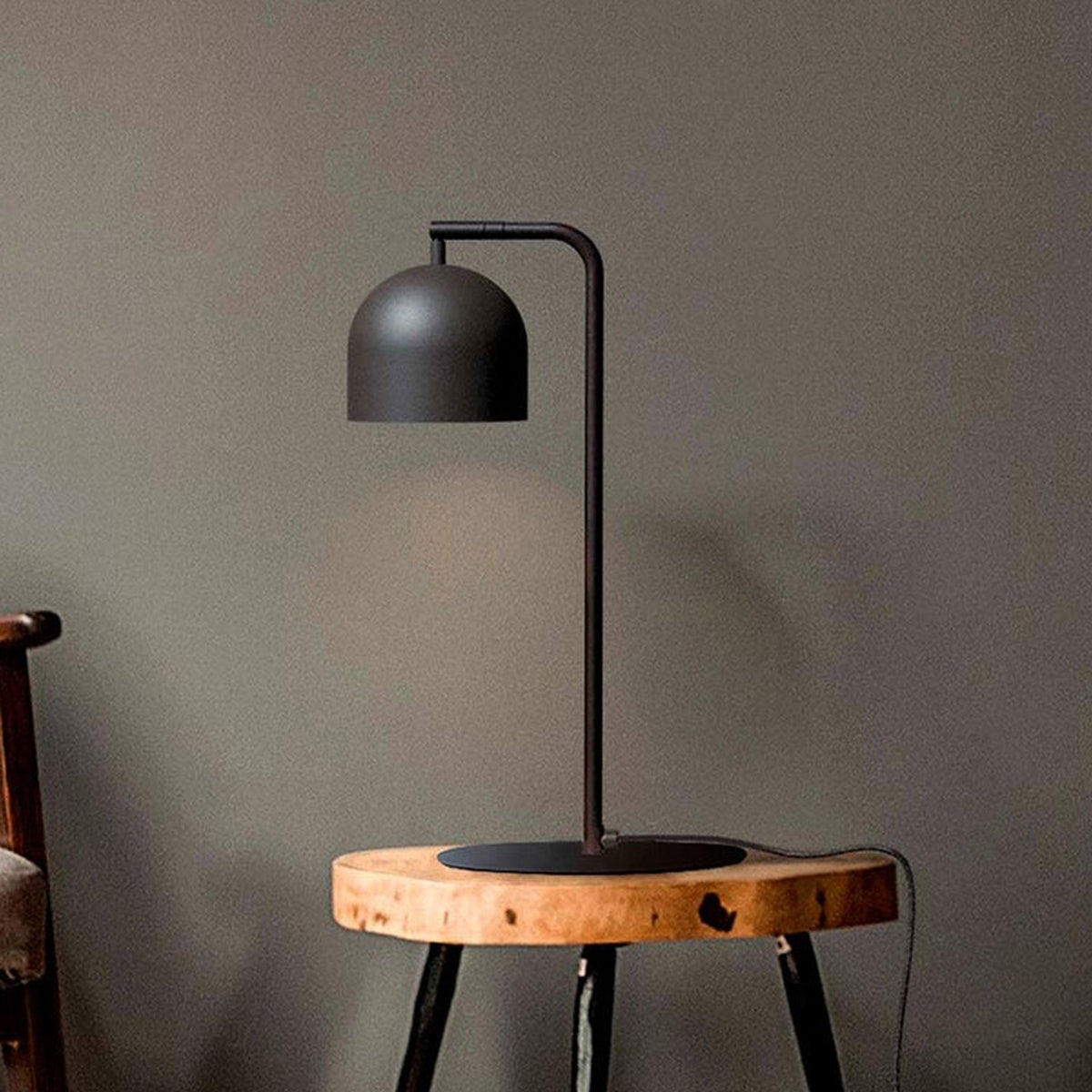 Rio Articulated Dome Adjustable Table Lamp in matt black, with slim iron stem, round base and hooked arm holding a dome shade, shown on a wooden stool.