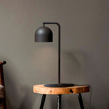 Rio Articulated Dome Adjustable Table Lamp in matt black, with slim iron stem, round base and hooked arm holding a dome shade, shown on a wooden stool.