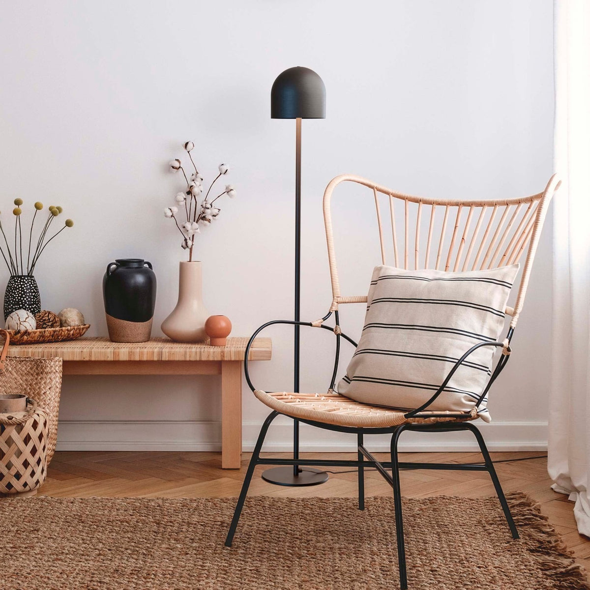 Rio 2 Light Dome Floor Lamp in matt black, slim stem and round base, shown beside a rattan chair in a living room with rug and side table.