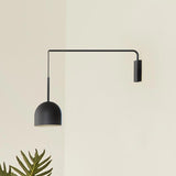 Rio Single Arm Dome Wall Light in matt black iron, with a slim right-angled arm from a rectangular wall plate and a cable-hung dome shade, shown against a plain wall near a potted plant.