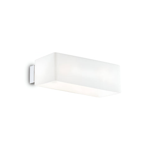 The Sage Light Wall Light - White, featuring a frosted glass diffuser and a sleek metallic base, is mounted on a white wall. Its minimalist design emits a soft, diffused glow that enhances the ambiance.