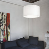 A minimalist living room exudes modern elegance, showcasing a large Marquise 3 Light Pendant in white, suspended by adjustable steel cables. The space is complemented by a black sofa and an abstract painting in red, black, and yellow. A white sculpted mantelpiece is partially visible on the adjacent wall.