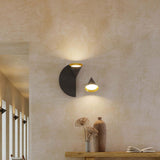 Rubi wall light duo in matt black and gold with cone-shaped opal glass shades on a half-disc and triangle back plate, mounted on a textured wall above a console table.
