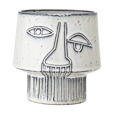 Sacad stoneware plant pot in white, featuring a raised-line face design with one open eye, one closed eye, a long nose, and ribbed footed base, shown on a plain background.