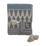Milas Cotton Throw in blue, folded to show a woven zigzag border, stacked bar and diamond motifs, striped edging, and tasselled corners, on a white background.