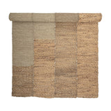 Enzov Seagrass Rug 245x150cm in Natural, partially rolled, showing four braided panels in varying earthy tones with visible stitched seams, on a plain white background.