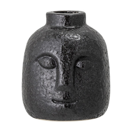 Eliot Stoneware Candle Holder in black, a small face-shaped taper holder with relief eyes, nose and smile, textured glossy finish, on a plain white background.