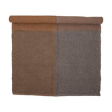 Rodin Jute Rug 200x140cm in Brown, partly rolled to show a diagonal twill weave in two colour-block shades of brown, on a plain white background.