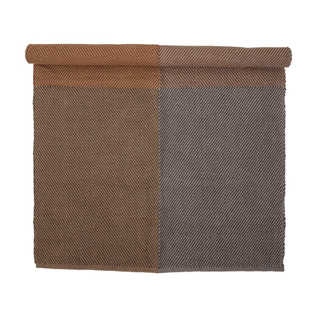 Rodin Jute Rug 200x140cm in Brown, partly rolled to show a diagonal twill weave in two colour-block shades of brown, on a plain white background.