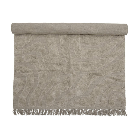 Elaine Wavy Cotton Rug 210x150cm in natural, partially rolled to show a tufted wavy pattern on flat-woven cotton with fringed edge, on a plain background.