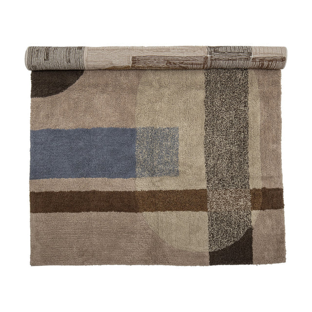 Zofia Geometric Cotton Rug, 200x140cm, partly rolled, showing a tufted beige rug with blue, brown and speckled grey geometric blocks on a plain white background.