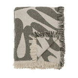 Alk Cotton Throw in green, folded showing a woven abstract leaf pattern in olive and cream with fringed edges, on a plain white background.