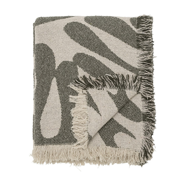 Alk Cotton Throw in green, folded showing a woven abstract leaf pattern in olive and cream with fringed edges, on a plain white background.