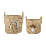 Set of 2 beige round woven water hyacinth kids storage baskets with handles, one with a stitched rainbow motif and the smaller featuring a mushroom design.