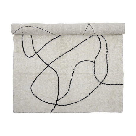 Viga Cotton Rug 180x120cm in white, partly rolled, showing a tufted black abstract line pattern on a soft white shaggy pile, shown against a plain background.