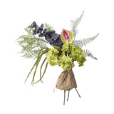 Poetry Artificial Bouquet in Green featuring large green hydrangea heads, dark veined orchid sprays, a pink anthurium, ferns and trailing foliage, wrapped in paper, on a white background.