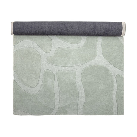 Darlington Wool Rug 200x130cm in green, partly rolled to show the dark grey woven backing, with a tufted pebble-shaped pattern in tonal pile heights, on a plain white background.