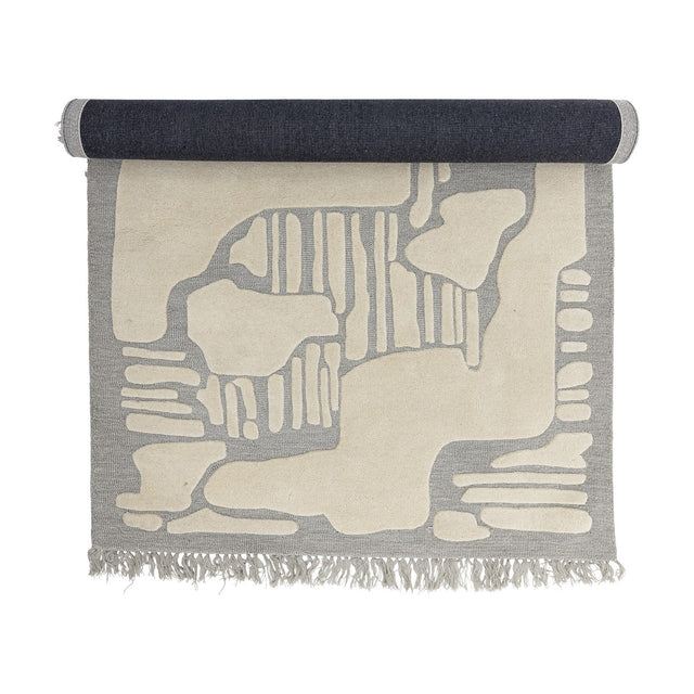 Napoli Wool Rug 200x140cm in grey, partly rolled, showing an abstract raised pattern in ivory with fringed edges on a white background.