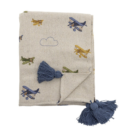 Plane Cotton Throw in beige, folded cotton blanket patterned with biplanes and outlined clouds, finished with chunky blue corner tassels, shown on a plain white background.