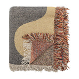 Arni Throw in Multi, a woven throw with a bold black and beige curved colour block design, folded corner revealing a speckled rust-toned reverse, finished with a thick multicoloured fringe.