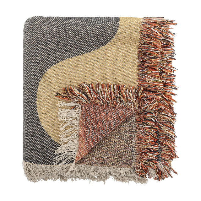 Arni Throw in Multi, a woven throw with a bold black and beige curved colour block design, folded corner revealing a speckled rust-toned reverse, finished with a thick multicoloured fringe.