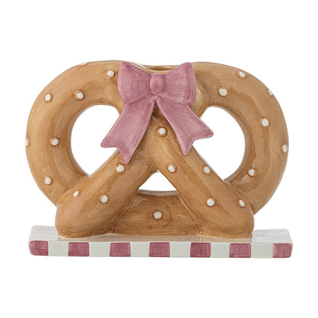 Ceramic pretzel-shaped candle holder in brown with raised dots, a pink bow at the centre, and a pink-and-white striped base, shown on a white background.