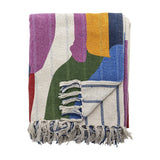 Artista Cotton Throw in Multi, folded to show abstract colour-block shapes in purple, green, blue and yellow with knotted fringe tassels, on a plain white background.