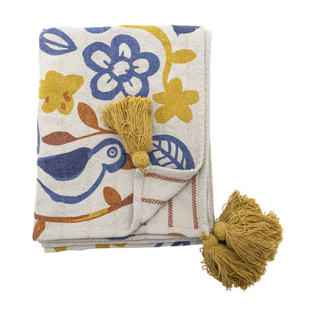 Figuria Cotton Throw in multicoloured folded with mustard corner tassels, featuring printed flower, leaf and bird motifs in blue, yellow and rust on a cream background.