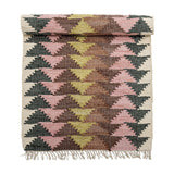 Desmond Geometric Cotton Rug, 180x80cm, with a mirrored triangle pattern in pink, mustard, brown and dark green on cream, fringed edges, shown rolled at the top on a white background.