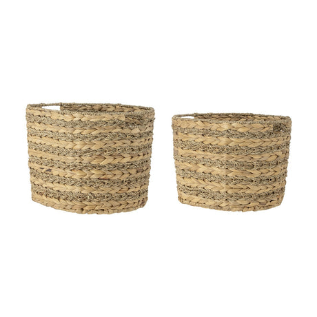 Indra Water Hyacinth Baskets, set of two oval woven storage baskets with ribbed texture from alternating plaited and twisted bands, natural finish, shown on a plain white background.