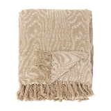 Okapi Cotton Throw in beige, folded with a wavy woven pattern in two tones and knotted fringe edge, shown against a plain white background.