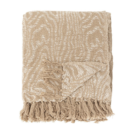 Okapi Cotton Throw in beige, folded with a wavy woven pattern in two tones and knotted fringe edge, shown against a plain white background.
