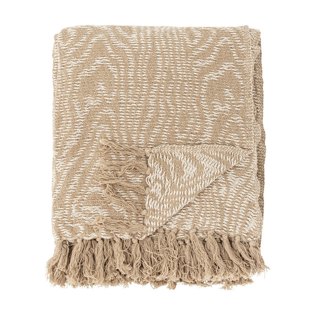 Okapi Cotton Throw in beige, folded with a wavy woven pattern in two tones and knotted fringe edge, shown against a plain white background.