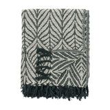 Ugento Leaf Cotton Throw in green, folded with a bold woven leaf pattern and knotted fringe edge, shown against a plain white background.